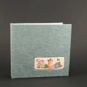 carnet avec couverture rigide en tissus type toile bleu-vert d'eau. incrustation d'un médaillon en céramique avec dessin renard