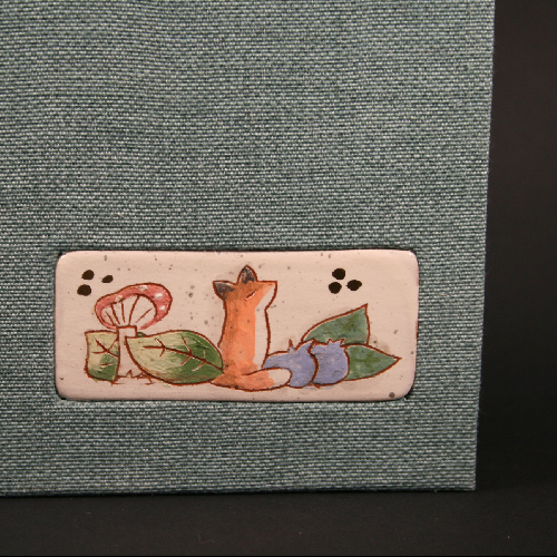carnet incrustation médaillon en céramique. couverture en tissus style toile couleur vert d'eau. détail du médaillon :dessin de renard